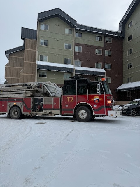 A fire truck parked in a snowy area near a multi-story building.