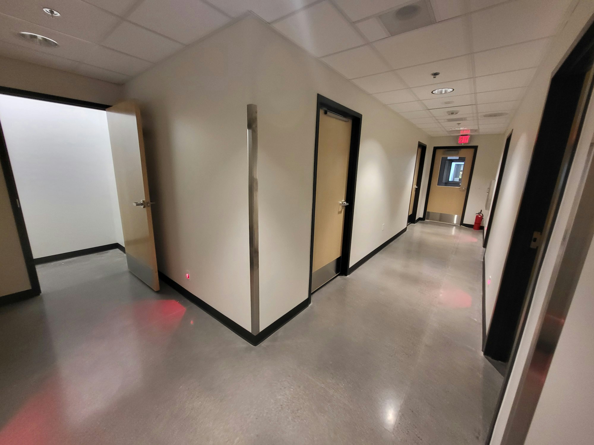 A hallway with doors, a reflective floor, overhead lights, an open door, and a fire extinguisher.