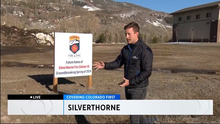 A man gesturing to a sign about the future Silverthorne Fire Station 10, with snowy hills in the background.