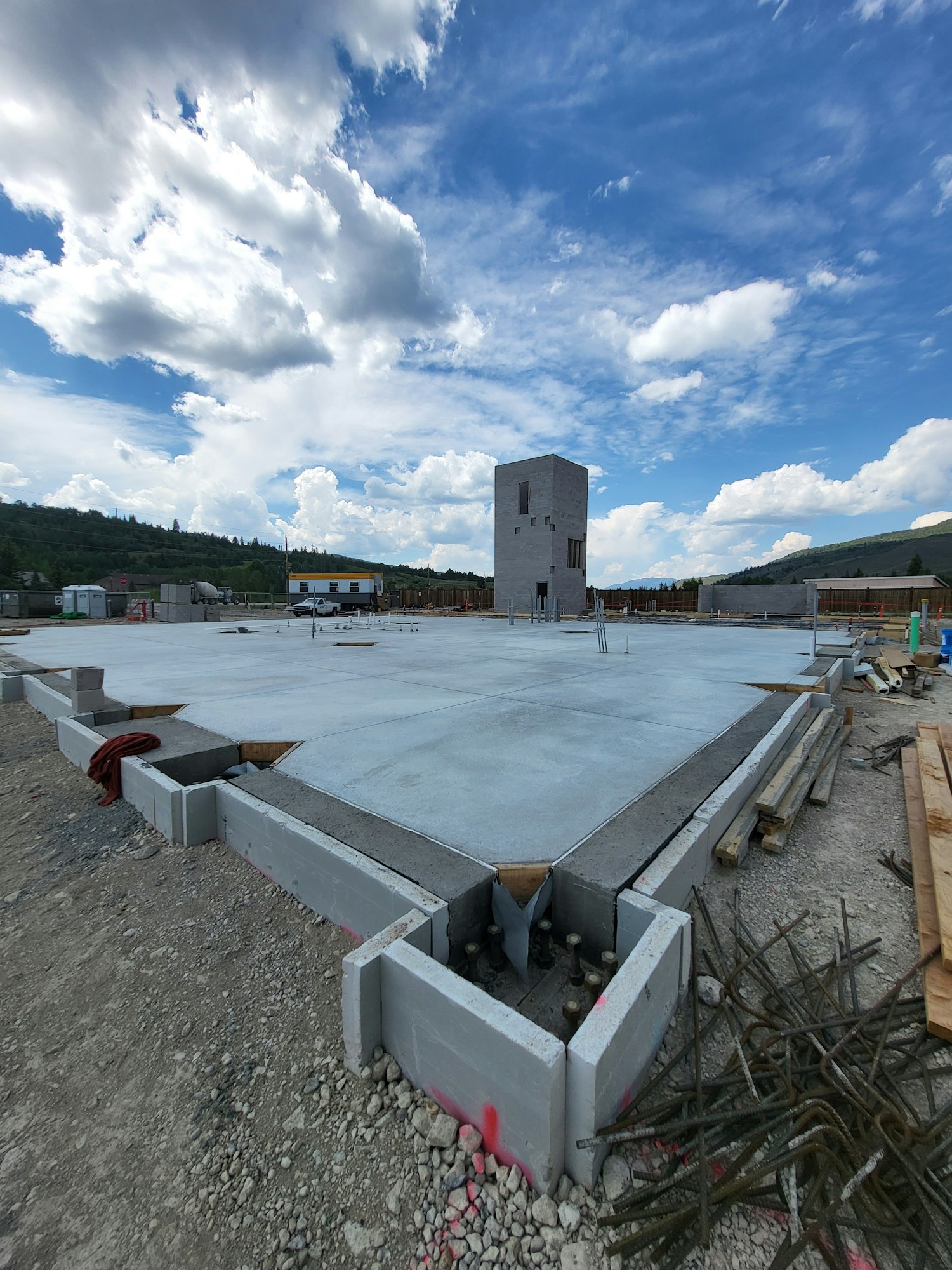 Construction site with concrete foundation, building materials, cloudy sky.