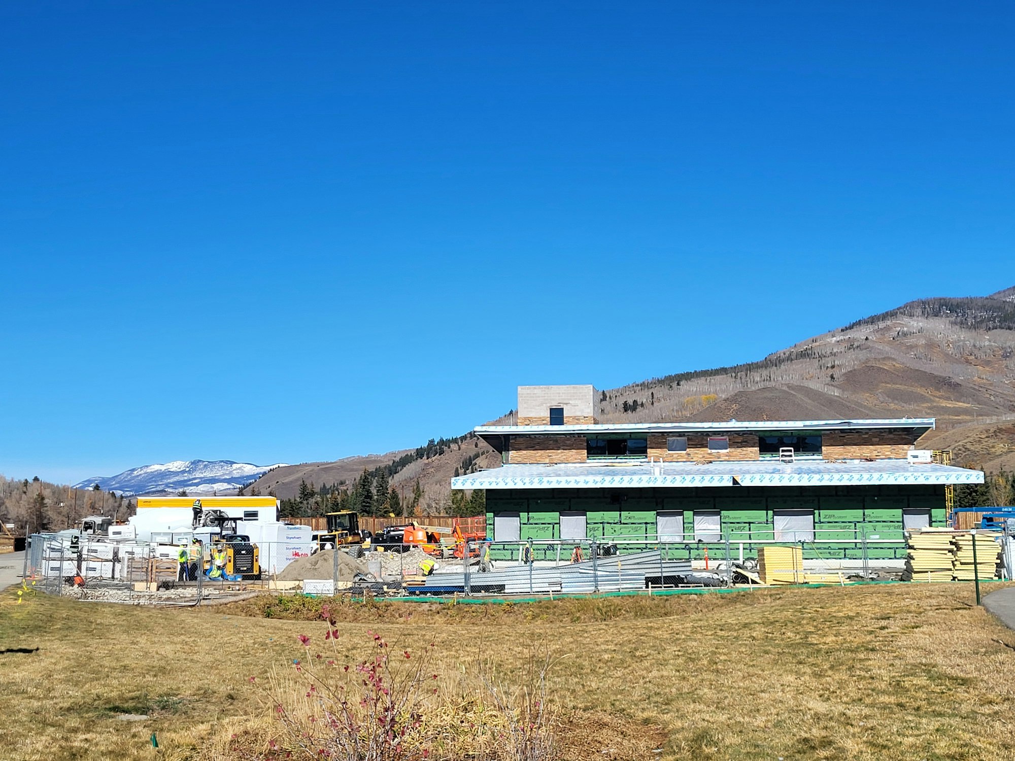 A construction site with materials in front of a building under renovation, set against a clear blue sky and mountainous backdrop.