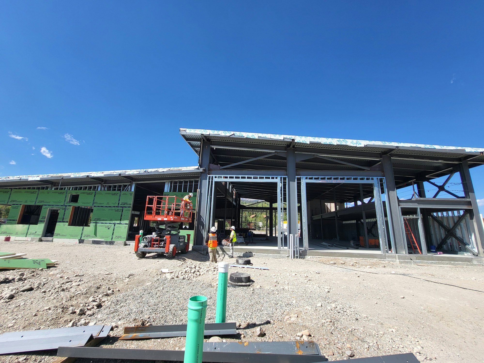 Construction site with steel framework, workers, and a scissor lift.