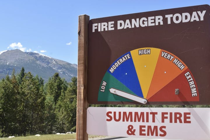 Fire danger sign with needle on "low," set against a mountain backdrop.