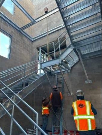 Construction workers on scaffolding, indoors, with one on ground looking up.