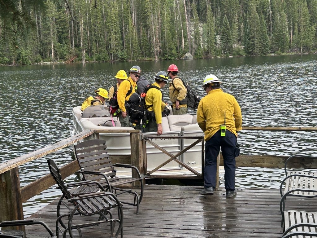 A group of people in yellow shirts prepares to board a boat at a lakeside, surrounded by trees.