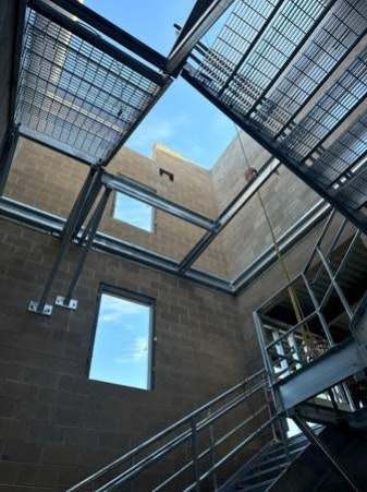 Metal staircase with grid-like structure, windows on a brick wall, under a clear sky.