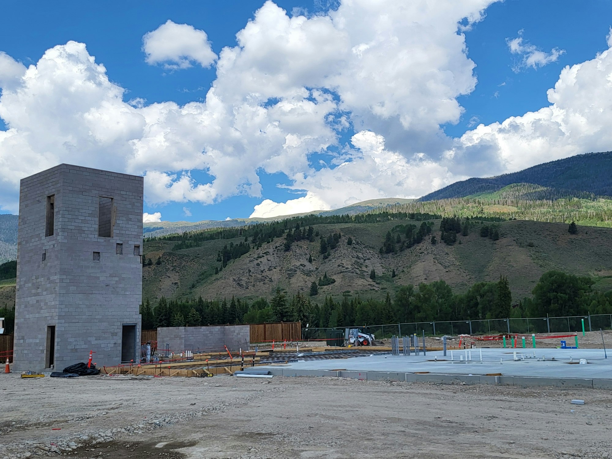 A construction site with a partially built structure, clear skies, and mountains in the background.