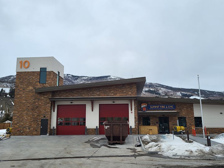 Fire station with two red doors, number 10, and "Summit Fire & EMS" sign, against a snowy mountain backdrop.