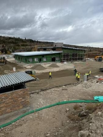 Construction site with workers, excavators, building under construction, and hilly background.