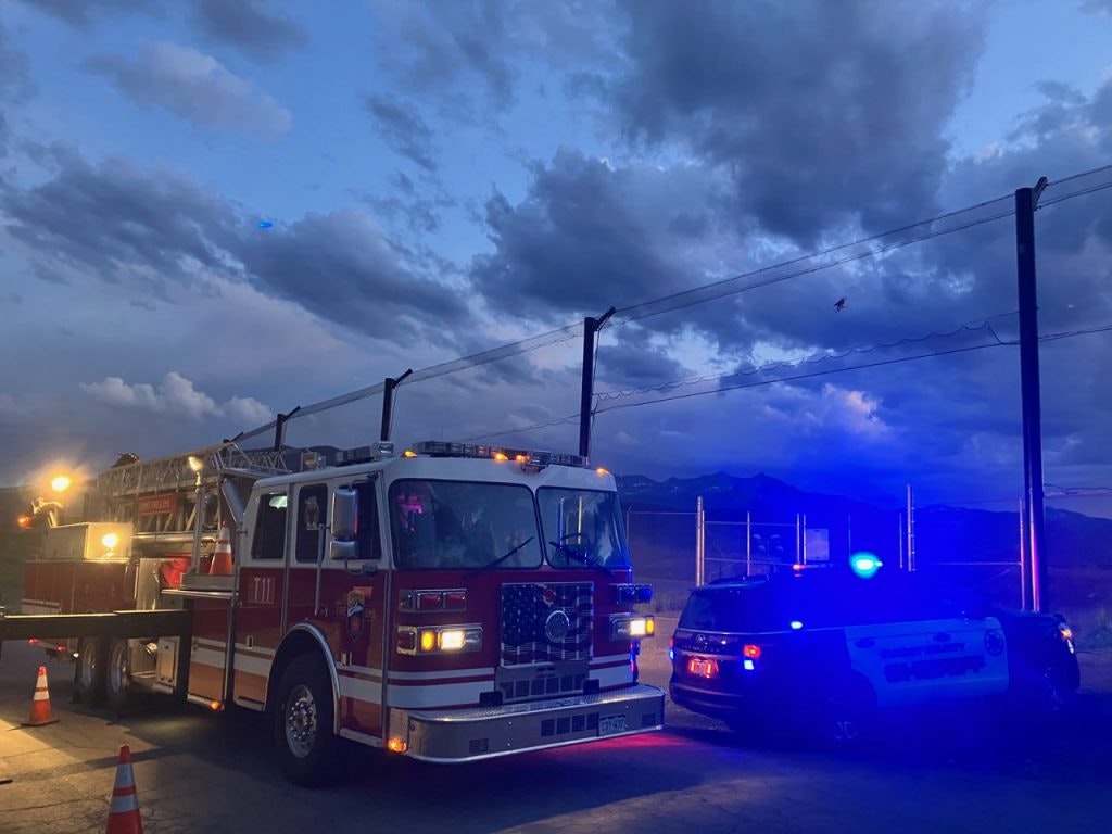 A fire truck and a police SUV with flashing lights parked near a fence under a cloudy sky.