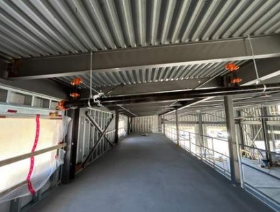 An empty industrial walkway with a metal structure, safety barriers, and suspended orange lights.