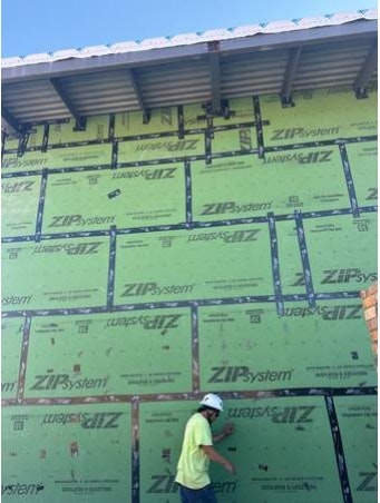 A worker near a wall with green ZIP System sheathing and branding.