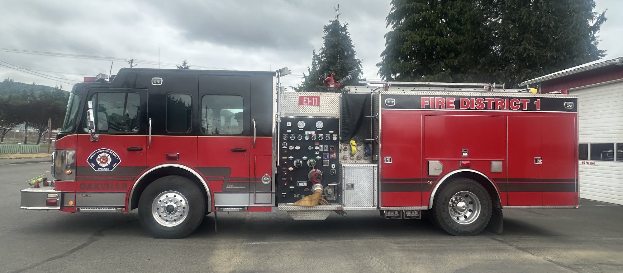 A red fire truck labeled "Fire District 1" is parked outside a building with trees in the background.