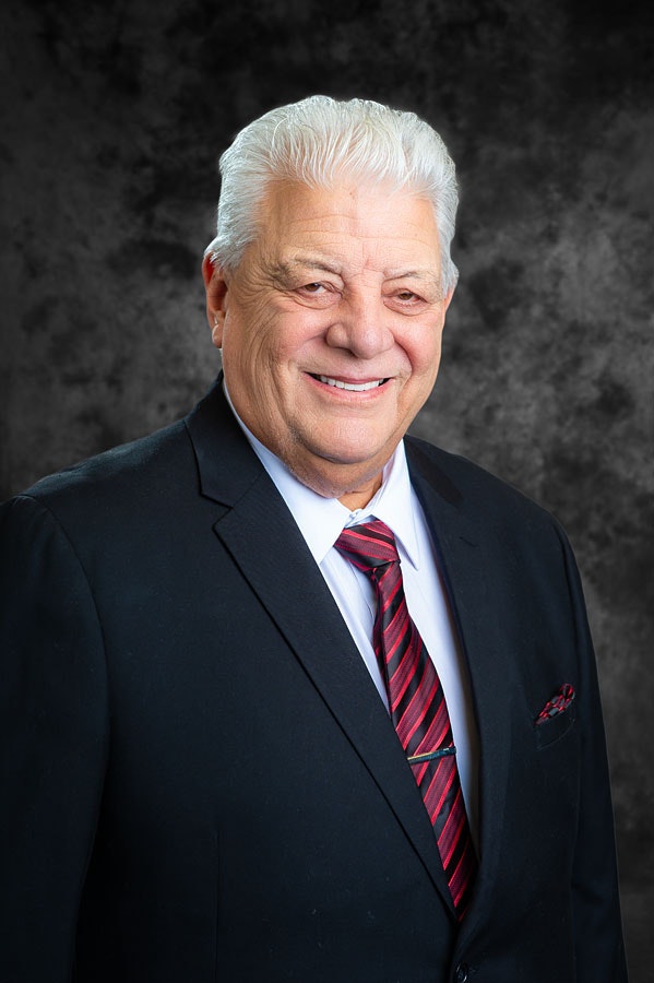 A smiling man in a suit and tie against a dark, textured background.