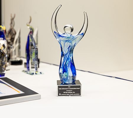 A blue and clear glass trophy in an abstract human shape, sitting on a table with a plaque for a communications award.