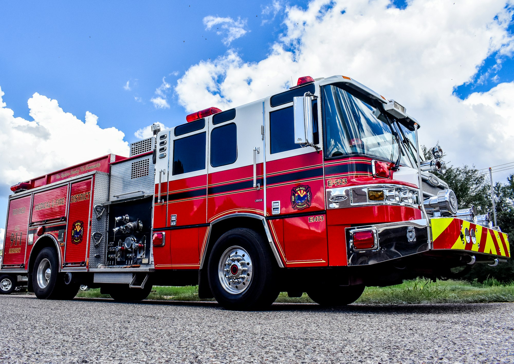A red fire truck parked on a street under a blue sky with clouds.
