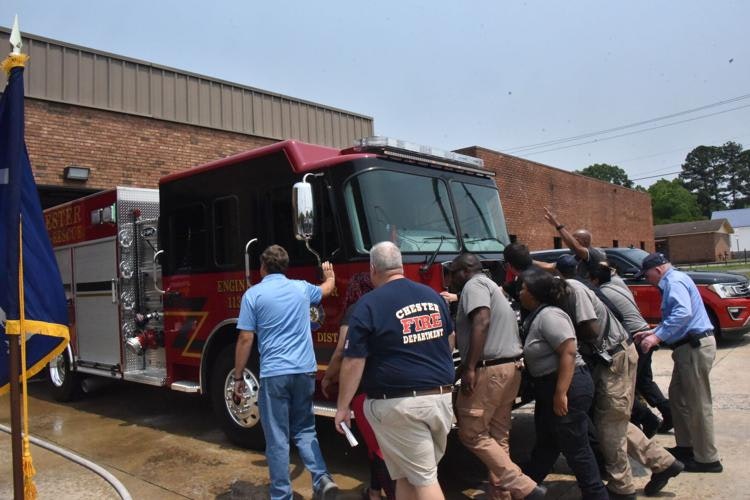A group of firefighters and officials gather around a fire truck, possibly for a ceremony or to celebrate the truck's arrival.