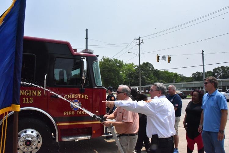 A group is celebrating near a fire truck, spraying water while a flag is displayed, likely at a community event or ceremony.