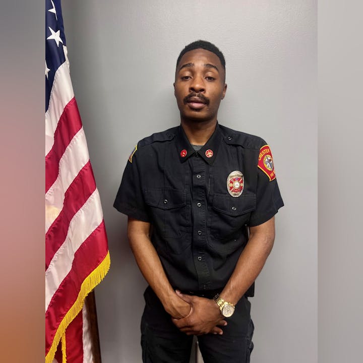 A person in a black uniform with badges stands beside a U.S. flag.