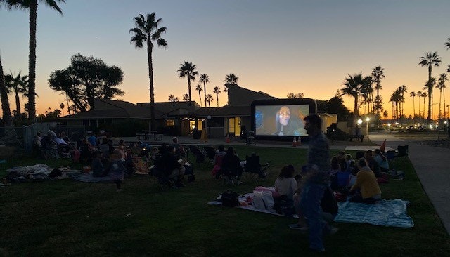 May contain: architecture, building, outdoors, shelter, palm tree, plant, tree, grass, people, person, nature, sky, concert, crowd, park, accessories, bag, handbag, urban, clothing, footwear, and shoe