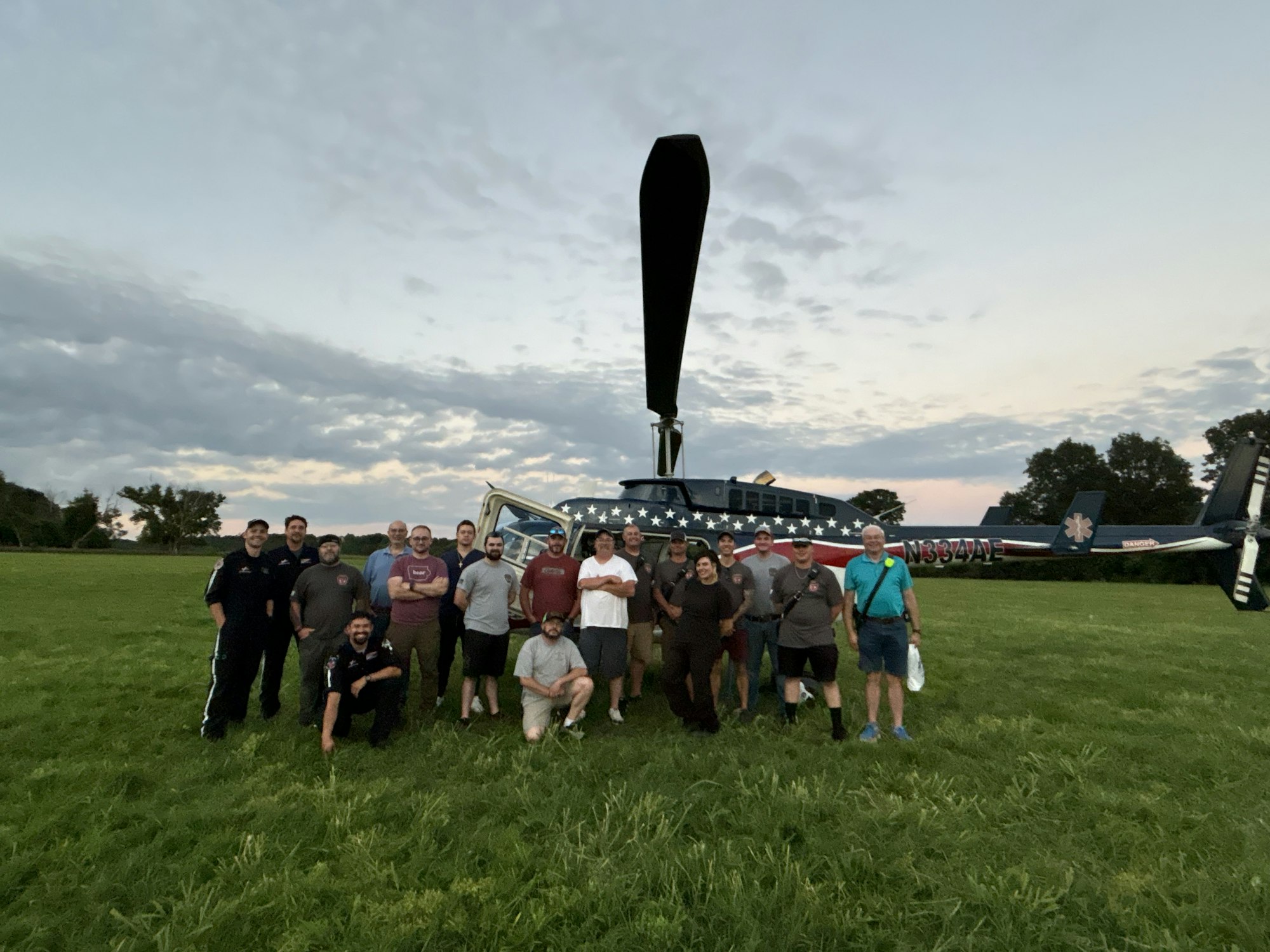 A group of people posing in front of a helicopter on a grassy field.