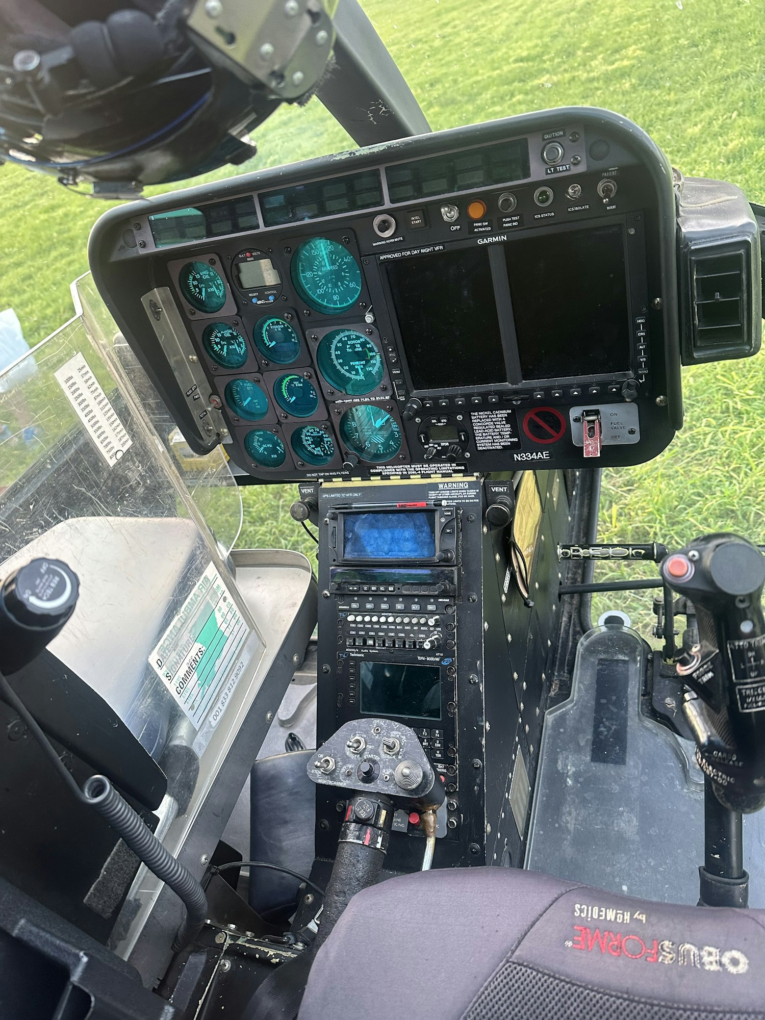 Helicopter cockpit with instruments, screens, and cyclic stick.