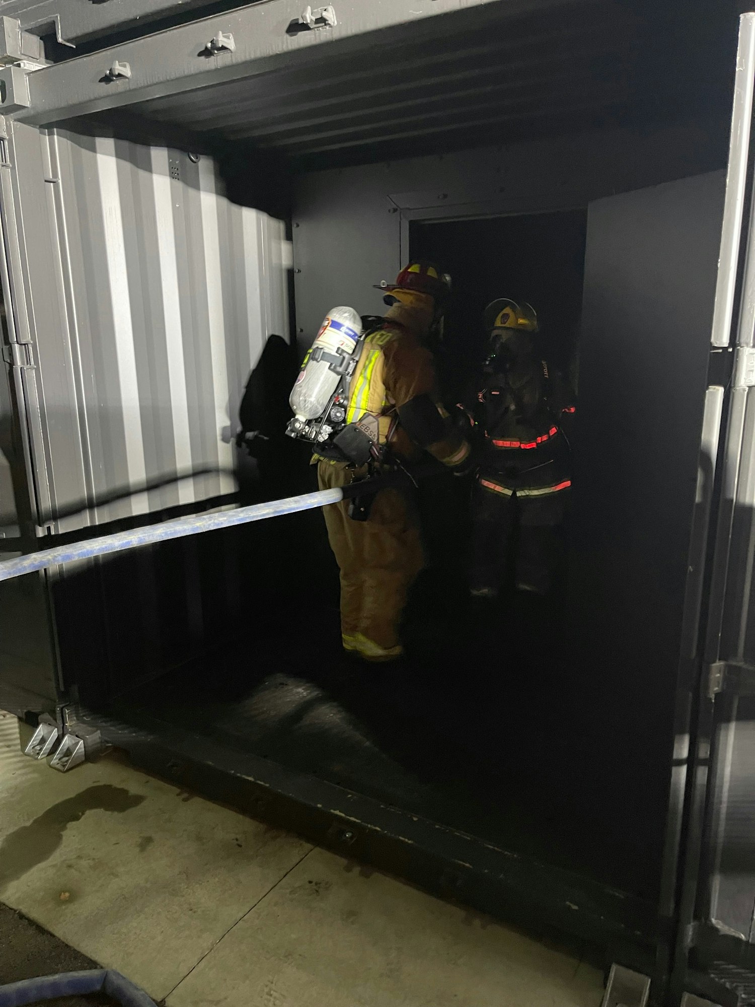 Firefighters descending a dark stairwell, equipped with gear and air tanks.