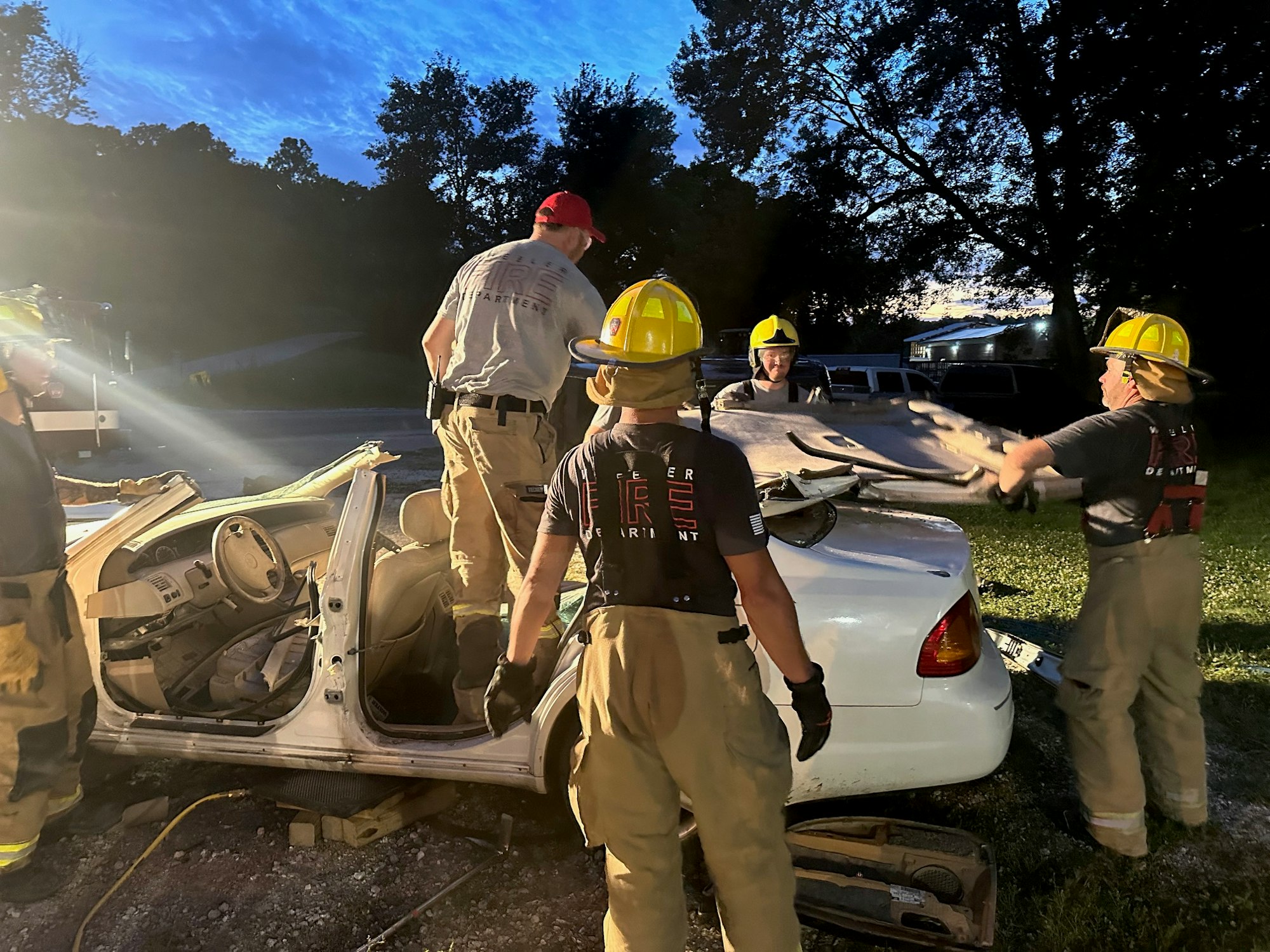 Firefighters training with overturned car at dusk.