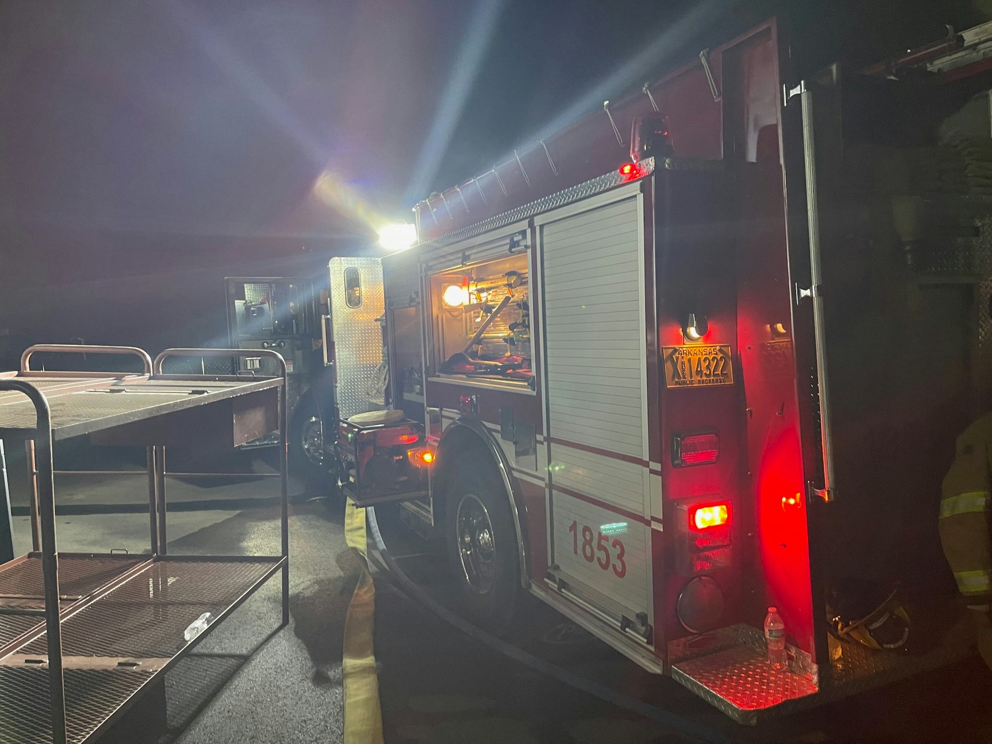 A fire truck at night with its compartment doors open and lights on, equipment visible, suggesting an emergency response scenario.