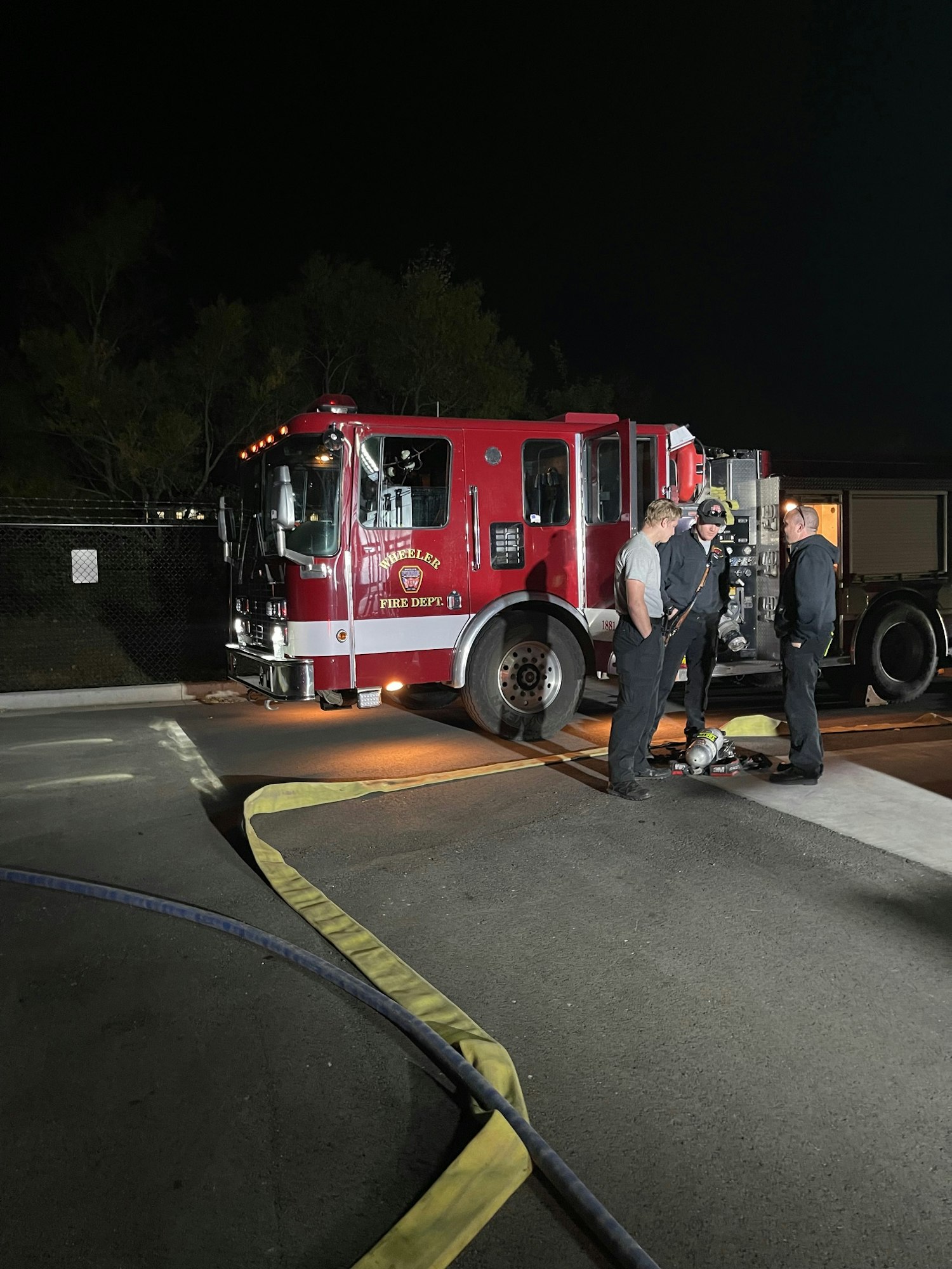 Fire truck and firefighters at night, hoses on ground, image rotated 90 degrees.