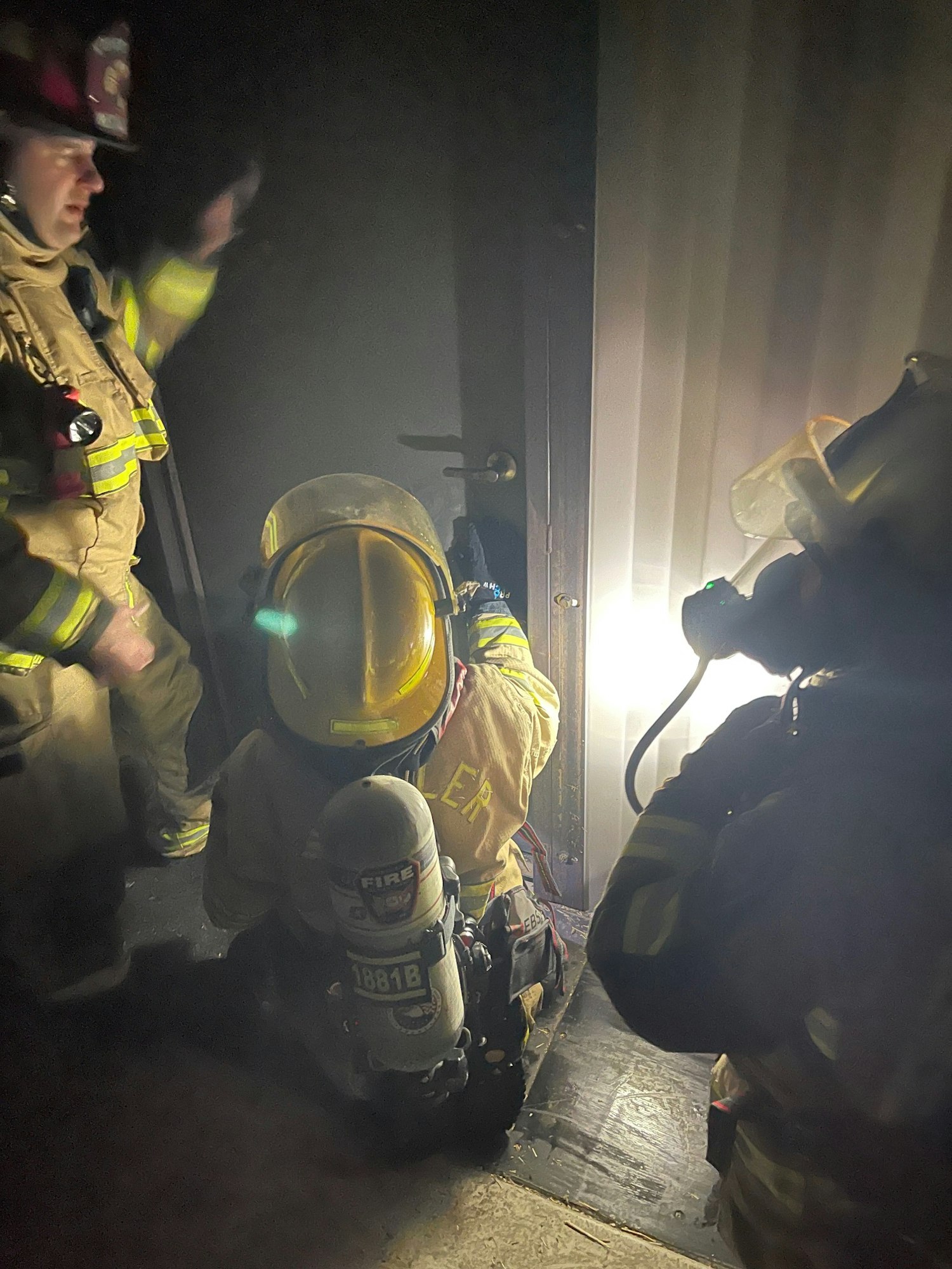 Firefighters working in close quarters, illuminated by a flashlight.
