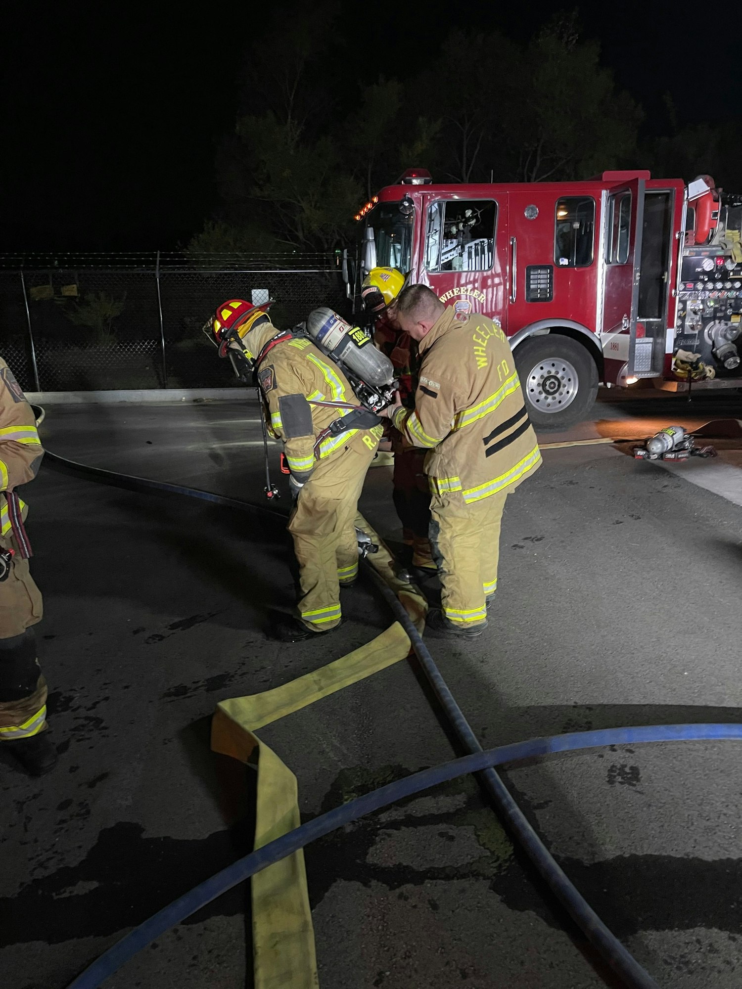 Firefighters with hoses by a fire truck at night.