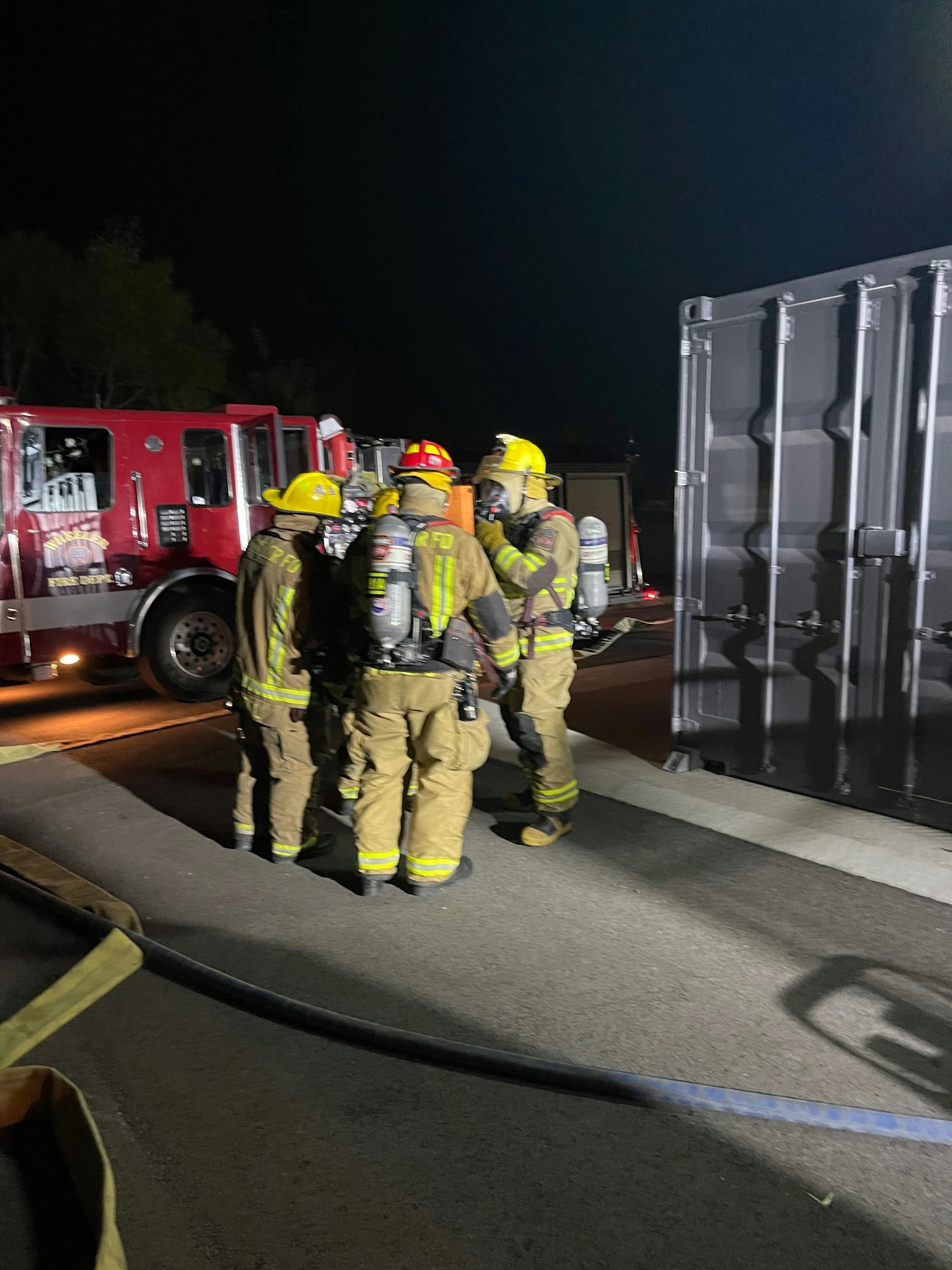 Firefighters in gear by a fire truck at night. Image is rotated.