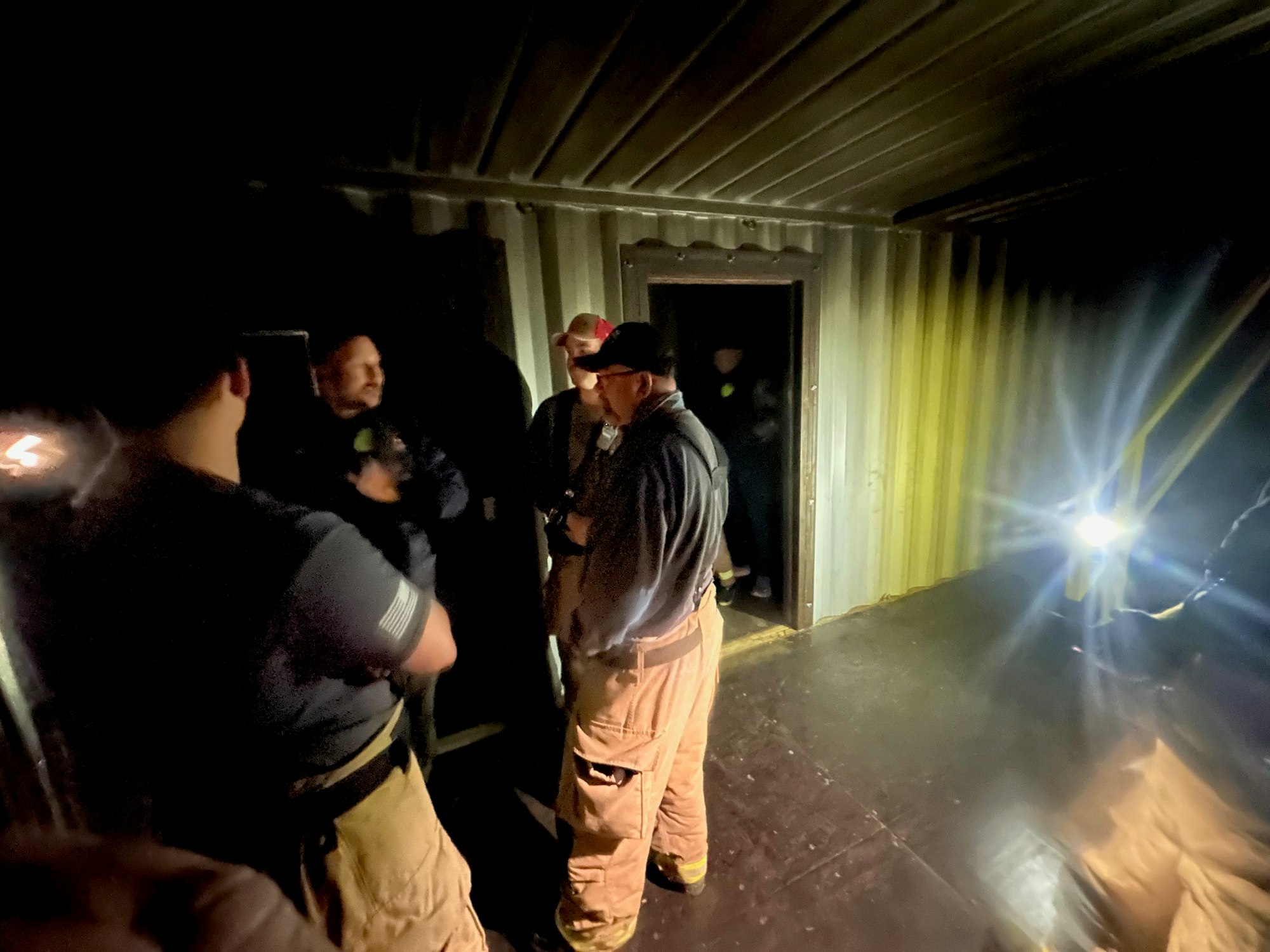 Group of people gathered in a dimly lit room, illuminated by a flashlight.