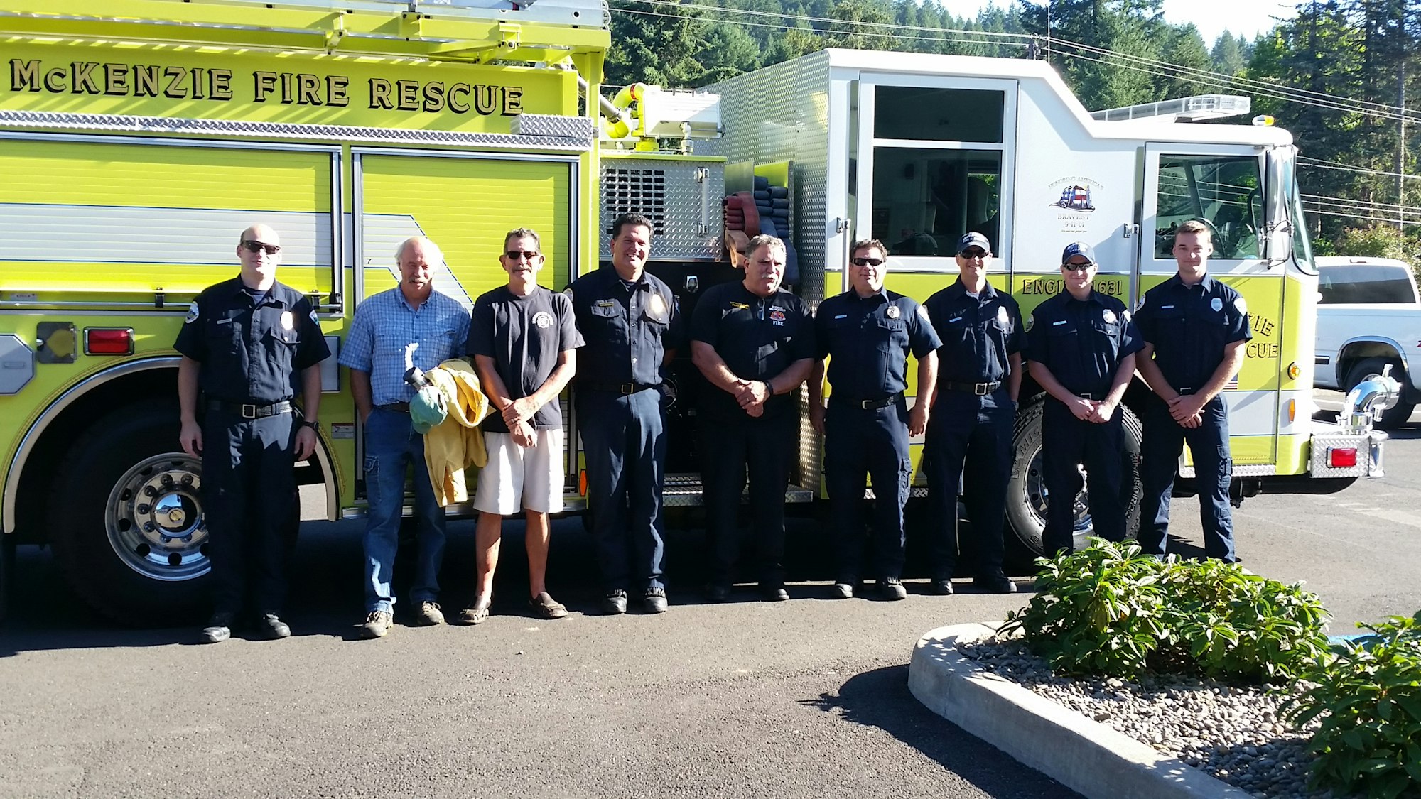 A group of firefighters stands in front of a yellow fire truck labeled "McKenzie Fire Rescue."