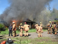 Firefighters in turnout gear in front of burn to learn structure on fire