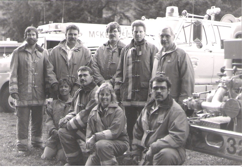 A group of people in firefighting gear poses in front of a fire truck.