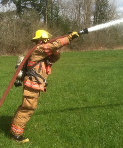 Firefighter in full turnout gear spraying water from fire hose