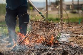 Person raking twigs and branches into a small outdoor fire.