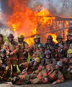Multiple firefighters in a group in front of burn-to-learn structure on fire