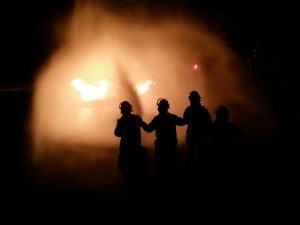 Silhouette of 3 firefighters spraying water and fire seen through water mist