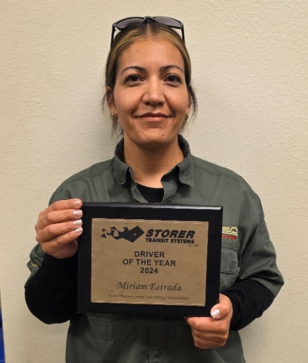 A person holding a "Driver of the Year 2024" plaque from Storer Transit Systems.