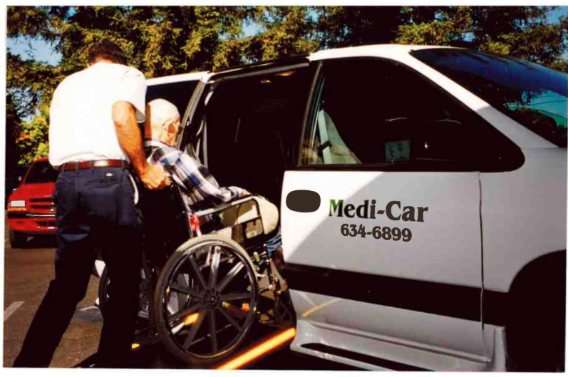 A caregiver assists a person in a wheelchair onto a van labeled "Medi-Car" with a phone number.