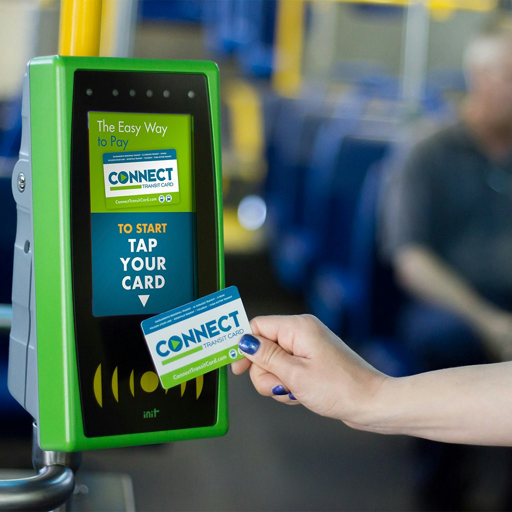 A hand is holding a CONNECT transit card near a contactless payment device on a bus, prompting to tap the card to start.