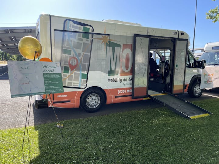 A mobility service van with a ramp, map design, and a welcome sign for zones 1 and 2 on display outdoors.