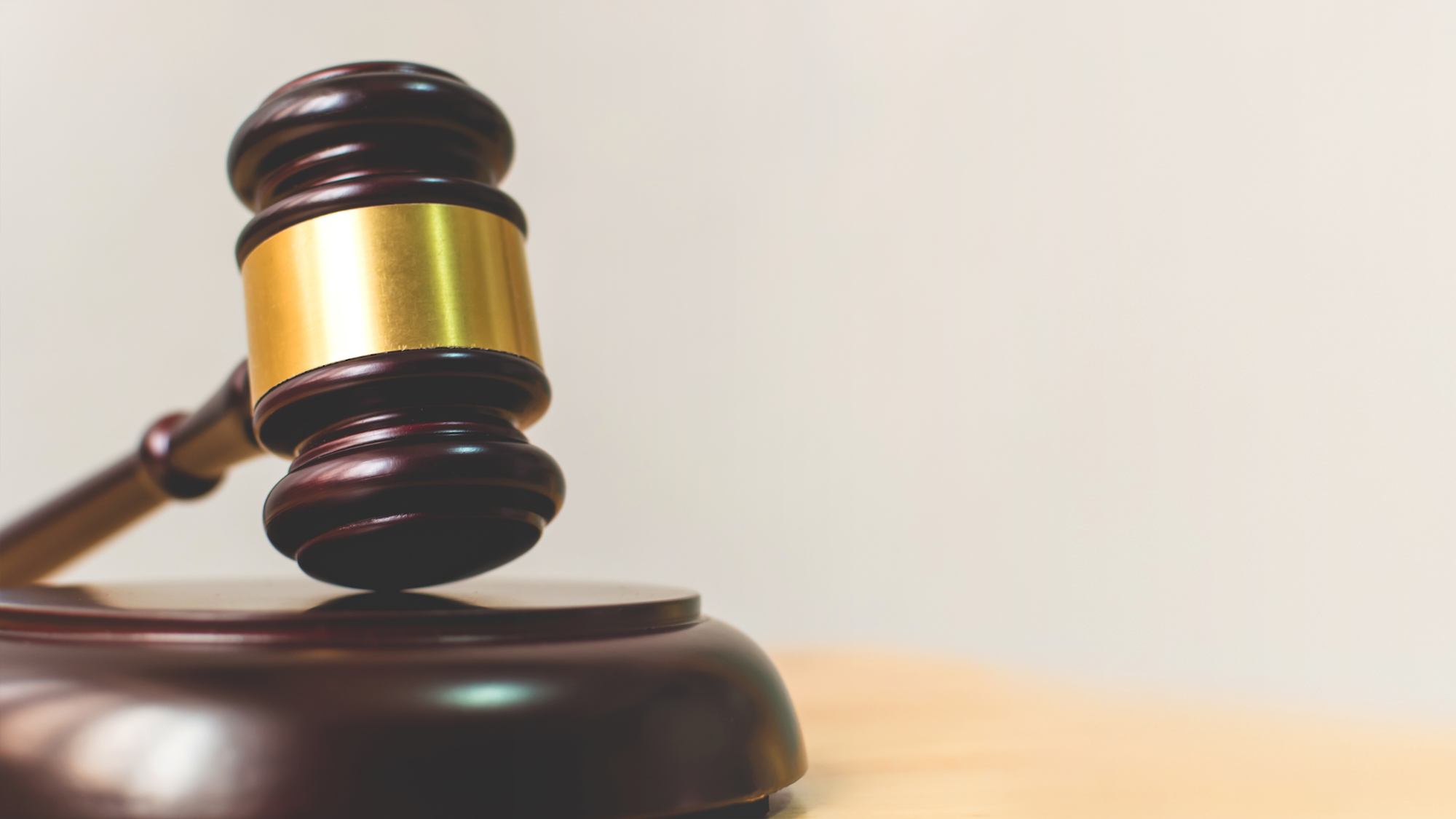 A wooden gavel with a golden band resting on a sound block against a neutral background.