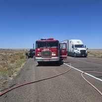A fire truck and a semi-truck are on a highway, with hoses laid out on the road.