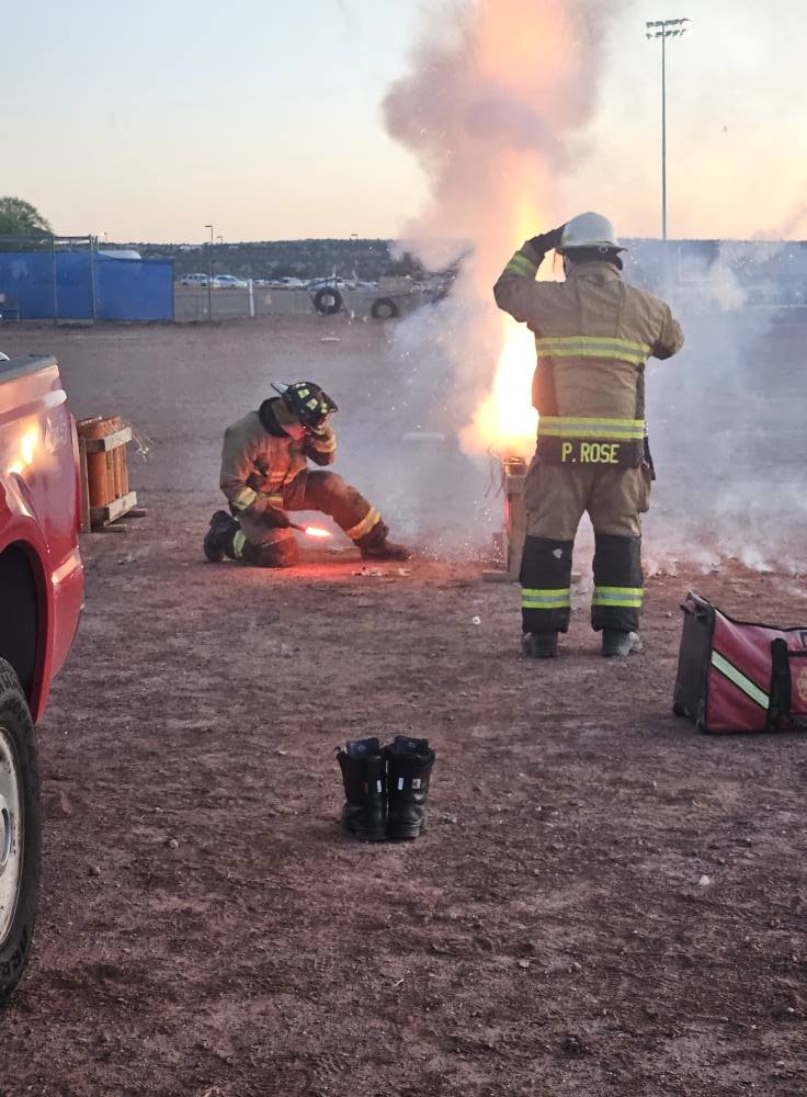 Firefighters dealing with a smoke and flame situation outdoors, with equipment and a pickup nearby.