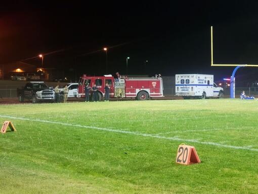 Football field at night with emergency vehicles, including a fire truck and ambulance, near the goalpost and 20-yard marker.