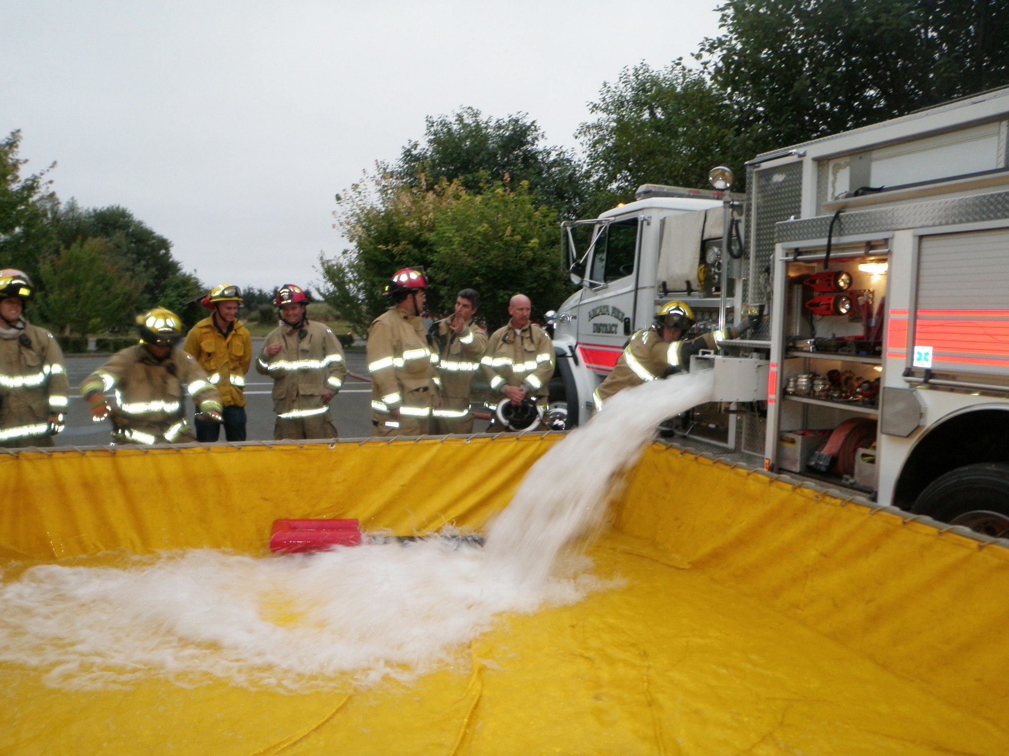 Group of firefighters observing Water Tender filling a portable tank.